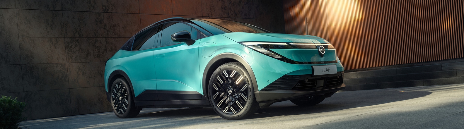 Nissan LEAF in Luminous Teal, Frontansicht schräg, modernes Design mit LED-Scheinwerfern, vor einer Holzwand.